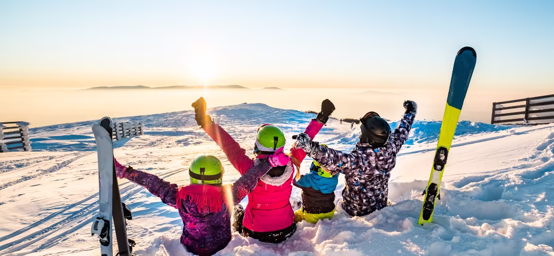 Une famille qui lèvent les bras face au couché du soleil en haut du montagne